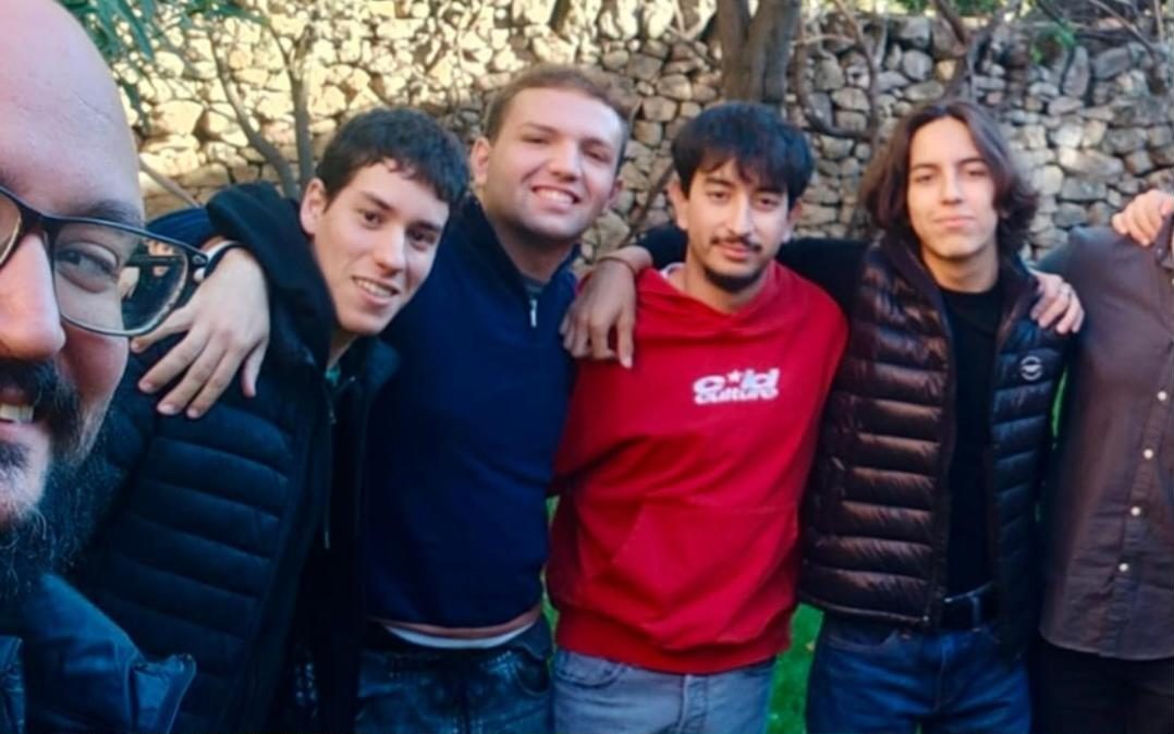 Jóvenes del grupo abrazados junto a un muro de piedra